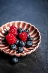 Raspberries and blueberries on a vintage porcelain plate on a dark stone table - healthy dessert