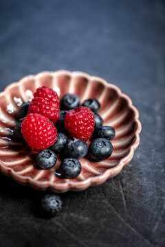 Raspberries and blueberries on a vintage porcelain plate on a dark stone table - healthy dessert