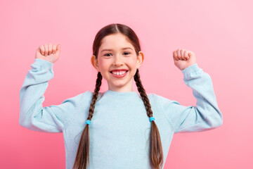Cheerful young girl with braided hair raising her arms in a pink backdrop showcasing happiness and...