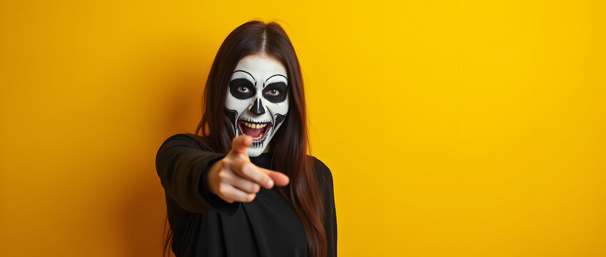 Femme moqueuse maquill&eacute;e en squelette montre du doigt le spectateur, isol&eacute; sur fond jaune 