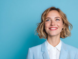 A young and pretty businesswoman with blonde hair wearing a light blue suit and white shirt, cheerfully looking to the side. Clean blue wall studio background 31008934 1
