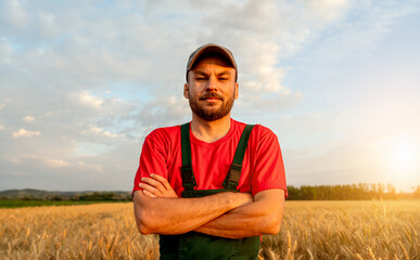 Portrait of male farmer with arms crossed in red t-shirt and bob overalls posing in cereal field