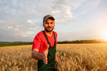 Confident farmer greeting partner with handshake in grain field