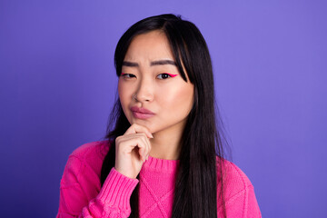 Portrait of a young stylish woman in pink sweater posing with thoughtful expression on a purple...