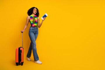 Young woman with curly hair wearing casual outfit holding travel essentials posing on a vibrant...