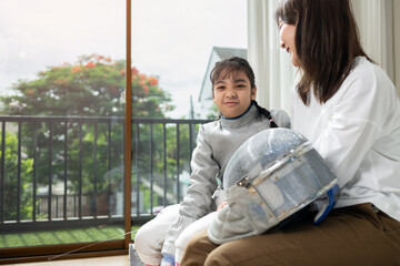 A girl in fencing gear with their mother preparing food and sports equipment