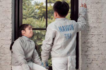 Before the tournament day, a boy and girl dressed in fencing gear are rehearsing in gym