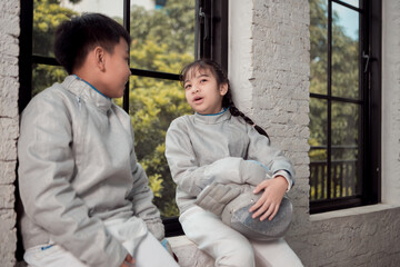 Before the tournament day, a boy and girl dressed in fencing gear are rehearsing in gym