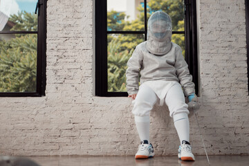 Before the tournament day, a boy dressed in fencing gear are rehearsing in gym