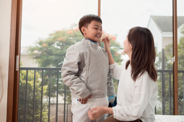 A boy in fencing gear with their mother preparing food and sports equipment