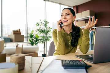 Successful young designer talking on the phone while working in a modern workspace with fashion...