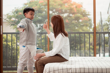 A boy in fencing gear with their mother preparing food and sports equipment