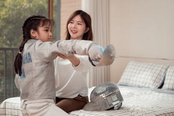 A girl in fencing gear with their mother preparing food and sports equipment