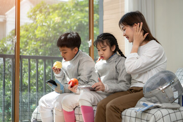 A girl and boy in fencing gear with their mother preparing food and sports equipment