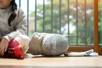 A girl in fencing gear resting before practicing fencing in preparation