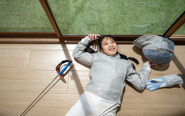 A girl in fencing gear is sitting and rest on the sidelines, exhausted from the training