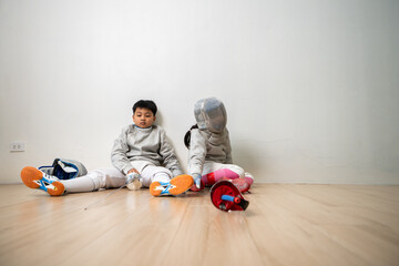 A girl and boy in fencing gear is sitting and rest on the sidelines, exhausted from the training...
