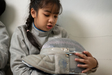 A girl in fencing gear is sitting on the sidelines, feeling disappoint for the unsuccessful game