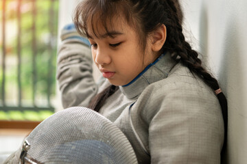 A girl in fencing gear is sitting on the sidelines, feeling disappoint for the unsuccessful game