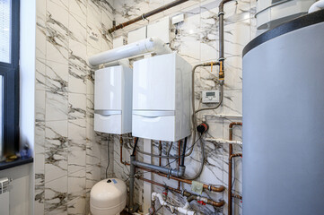 utility room features two white boilers, pipes, and a water heater against a marble-tiled wall