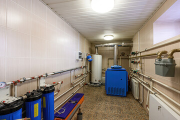 utility room with pipes, tanks, and equipment, illuminated by ceiling lights