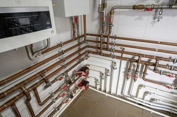 complex network of copper and white PVC pipes with valves and pumps against a tiled wall. Appears...