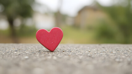 A red heart-shaped object on a textured surface with a blurred background