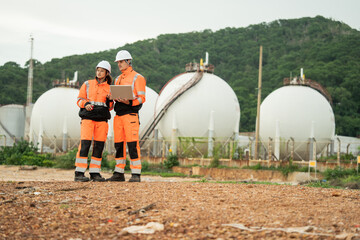 Two engineer workers review data on laptop, team discusses plans at energy plant, Petrochemicals factory, Storage tanks, construction site survey, Industrial site operation
