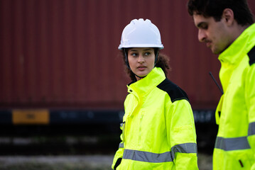 Engineers wearing safety uniforms performing site walk beside railway track near freight containers, two workers inspection logistics cargo.