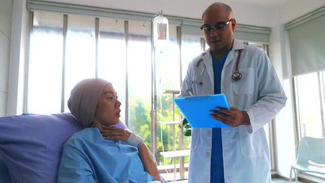 Asian woman patient describes her symptoms to an oncologist while sitting on a bed and looking at a man doctor in a lab coat in a hospital ward, health and medical care concept