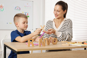 Cute boy learning letters with teacher at desk in school