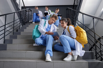 Medical students in uniforms studying together on stairs indoors, low angle view