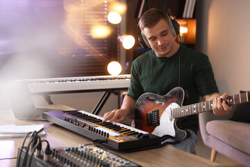 Man in headphones working with MIDI keyboard and guitar at table in home studio