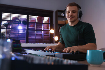 Smiling man in headphones working with MIDI keyboard at table in home studio, low angle view