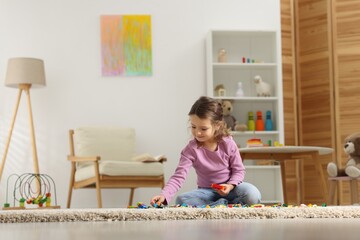 Cute girl playing with building blocks on floor at home. Space for text