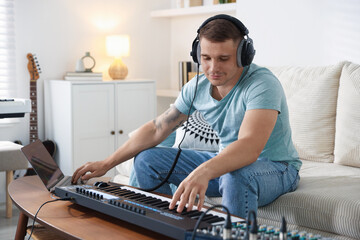 Man in headphones working with MIDI keyboard and laptop at table indoors