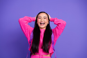 Cheerful young woman in pink sweater enjoying fun moments with hands on head on vivid purple...