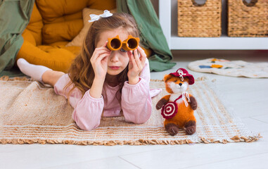 Cute little girl playing with toys sitting on the floor in a cozy children's room interior	
