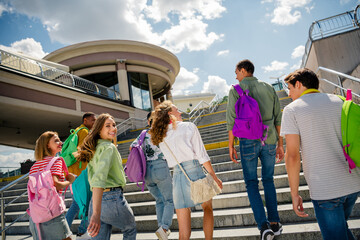 Group of young friends ascending city steps on a sunny day in casual attire with colorful backpacks