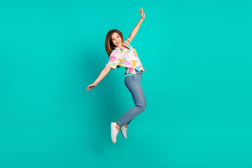 Playful young woman in casual colorful outfit jumps cheerfully against a vibrant teal background...