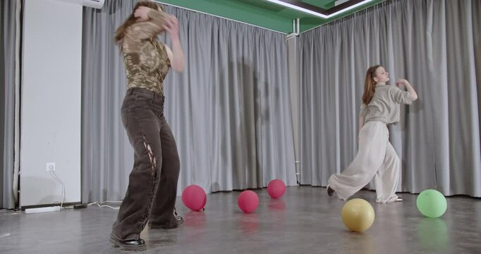 Two young women perform a modern dance in a studio. The video captures their energy, and synchronization in a spacious studio setting.