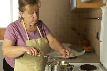 Senior woman in apron adding sweet butter to a pan to melt, making ghee