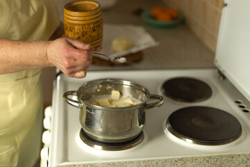 The hands of a senior woman add salt to the butter that is melting on the stove