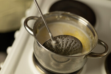 stirring sweet cream ghee in a saucepan with a metal spoon with holes