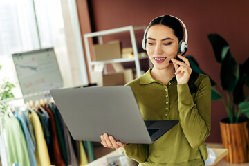 Starting a small business fashion designer in an green outfit holding a laptop and wearing a...