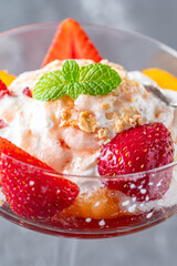 Ice cream with whipped cream, strawberries and peach in a glass tall glass on a gray background. Close-up. Copyspace