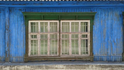 Old dilapidated wooden building. Green trim of white window on blue wall of house. Bright colors of...