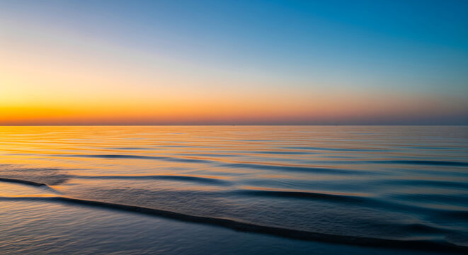 A tranquil sunset over a calm ocean with gentle waves lapping the shore