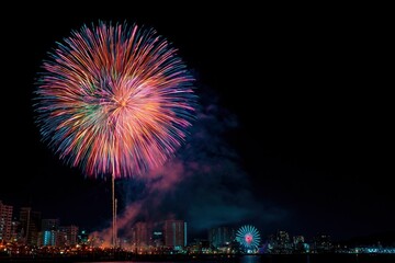 A vibrant firework bursts above a city skyline at night casting a colorful glow with smoke