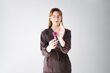 Young woman in glasses holding a pink otoscope and checking the light on her hand against a light background.